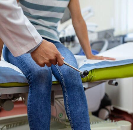 Doctor neurologist knocking on knee of patient with hammer in clinic closeup. Diagnosis of neurological pathology of knee reflex concept